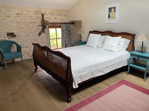 Une chambre Ă coucher avec un lit en bois, un mur en pierre, une fenĂȘtre avec des rideaux, une chaise et une lampe.