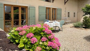 Ein Gebäude mit Kiesterrasse, einem Tisch mit Stühlen und einem Blumenbeet mit rosa Blüten.