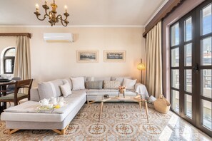 Una sala de estar moderna con un sofá modular, una mesa de centro, una araña y ventanas amplias.