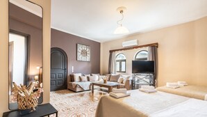 A hotel room with a bed, a sofa, a TV, a coffee table, and a decorative mirror. - Apartment 'Afentika Grand Flat' with Mountain View, Wi-Fi and Air Conditioning (Archangelos)