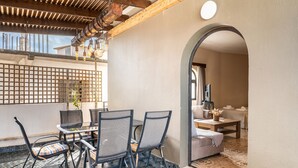 An outdoor patio with a table and chairs, a wooden ceiling, and a view into the interior. - Apartment 'Afentika Grand Flat' with Mountain View, Wi-Fi and Air Conditioning (Archangelos)