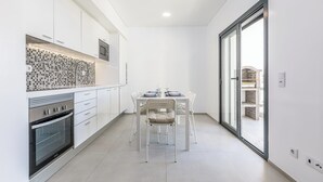 Eine moderne Küche mit weißen Schränken, einer gefliesten Spritzschutzwand und einem Essbereich mit Glastür zum Außenbereich.