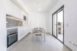 A modern kitchen with white cabinetry, a tiled backsplash, and a dining area with a glass door leading to an outdoor space. - Correeira Luxury Residence A (Albufeira)