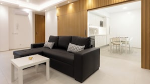 Ein modernes Wohnzimmer mit einer schwarzen Eckcouch, einem weißen Couchtisch und einem Essbereich mit weißem Tisch und Stühlen.