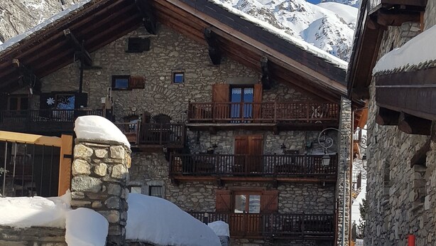 Ein Steinhaus mit hölzernen Balkonen und einem verschneiten Eingang.