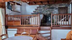 Ein rustikales Holzinterieur mit einer Essecke, die einen Tisch und Stühle, einen Kamin aus Stein und eine Holztreppe umfasst.