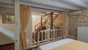 Un dormitorio con cama, escalera de madera, pared de piedra y radiador blanco.
