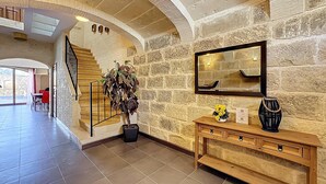 A spacious lobby with a stone wall, a wooden staircase, a large potted plant, a wooden console table with a mirror, and a view of the outdoor area. - Mia - Your Gozo Haven with Pool (Ix-Xagħra)