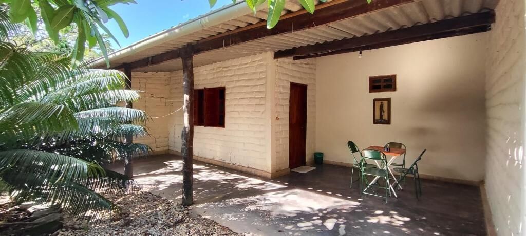 Un espacio al aire libre techado, con piso de concreto, una puerta de madera y una pequeña mesa con sillas.