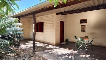 Un espacio al aire libre techado, con piso de concreto, una puerta de madera y una pequeña mesa con sillas.