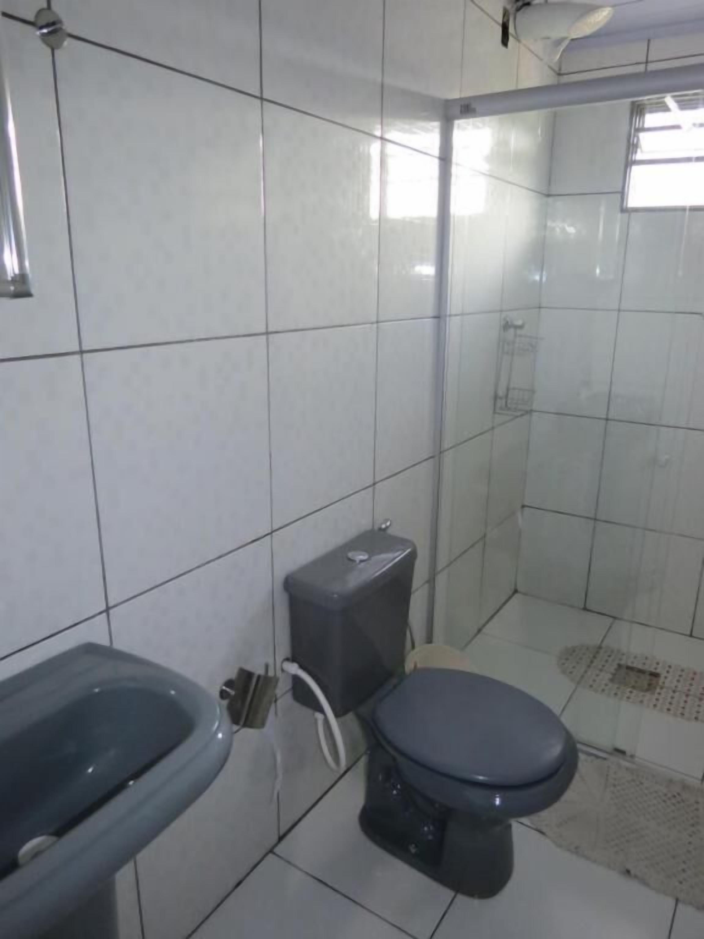A bathroom with white tiled walls, a toilet, a sink, and a shower area.