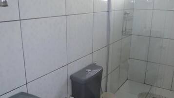 A bathroom with white tiled walls, a toilet, a sink, and a shower area.