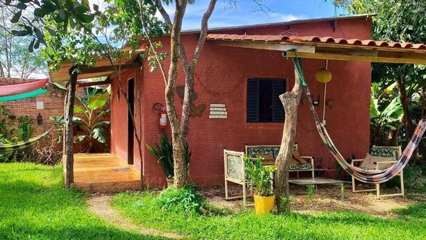 A small, rustic building with a red exterior, a wooden porch, and a hammock. - Pequizeiro Eco Pousada (Cavalcante)
