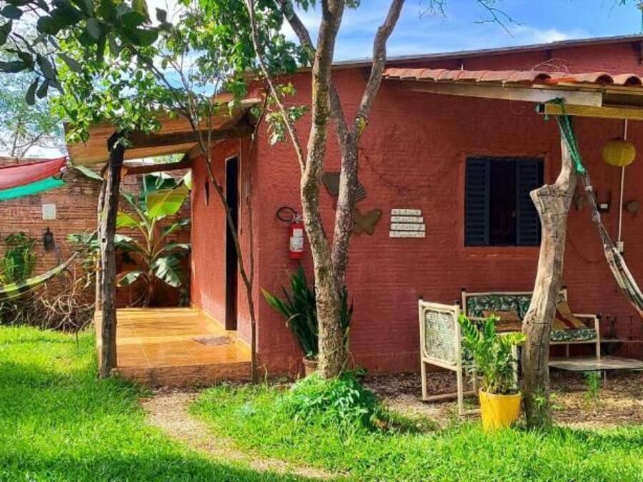 Um pequeno edifício rústico com fachada vermelha, varanda de madeira e uma rede.