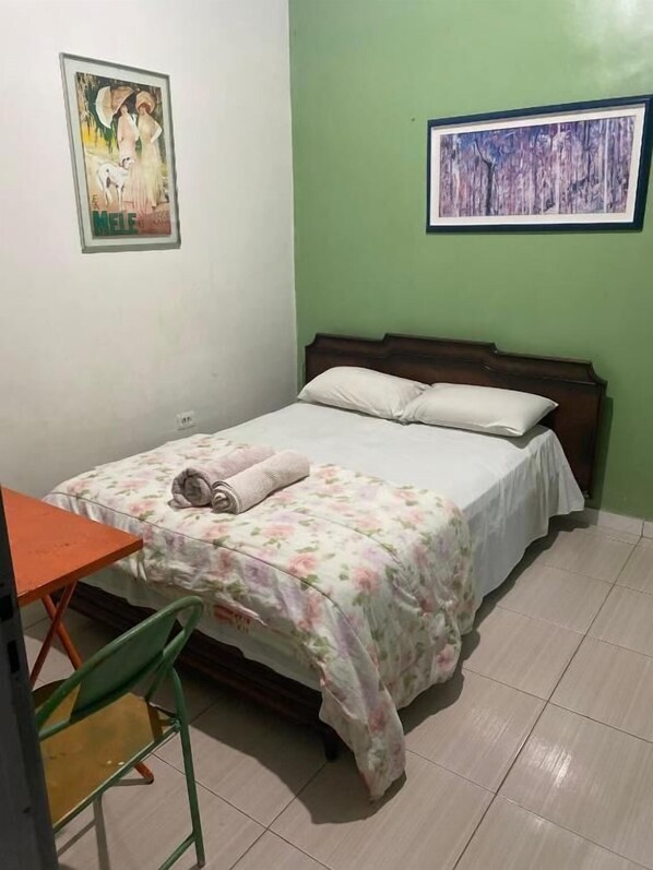 A bedroom with a bed, a chair, a small table, and two framed pictures on the walls.