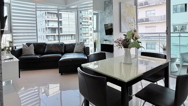 Una sala de estar moderna con un sofá de cuero negro, una mesa de comedor de vidrio y un ventanal con vistas a rascacielos.
