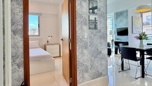 Un hotel moderno con una cama grande, una mesita de noche con lámpara, una pequeña planta en maceta y vistas a la ciudad por la ventana.