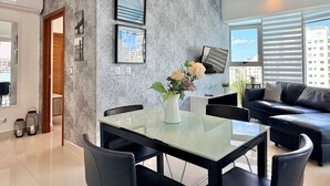 Un salón moderno con una mesa de comedor de vidrio, sofá de cuero negro y vistas a la ciudad a través de amplios ventanales.