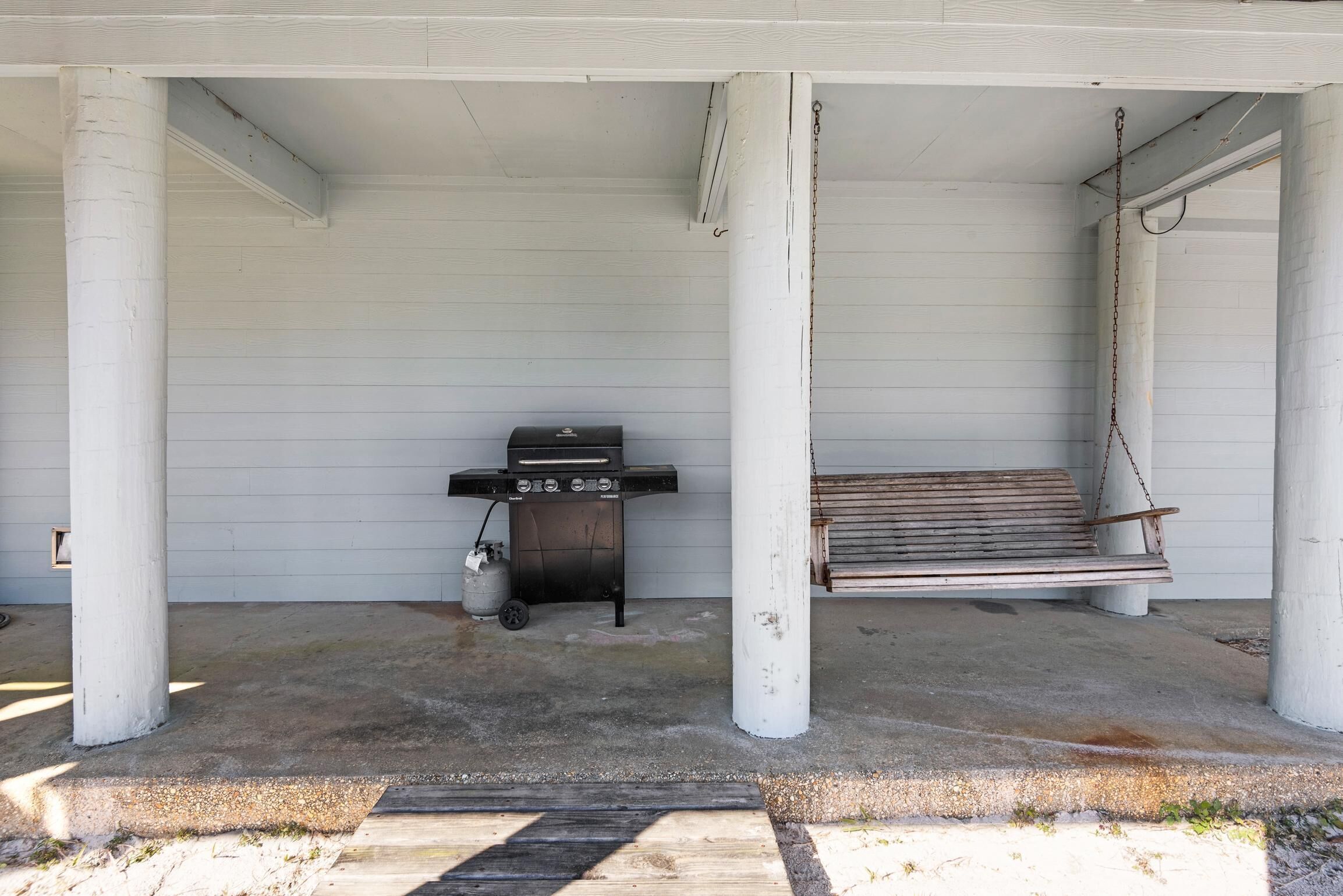 A covered porch with a grill and a swing.
