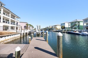 Eine Uferpromenade mit Holzsteg, wo Boote an der Wasserkante liegen und mehrstöckige Gebäude mit Balkonen zu sehen sind.
