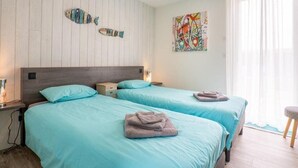 Une chambre d’hôtel avec deux lits, une tête de lit en bois, un tableau abstrait aux couleurs vives et une fenêtre ornée de rideaux légers.