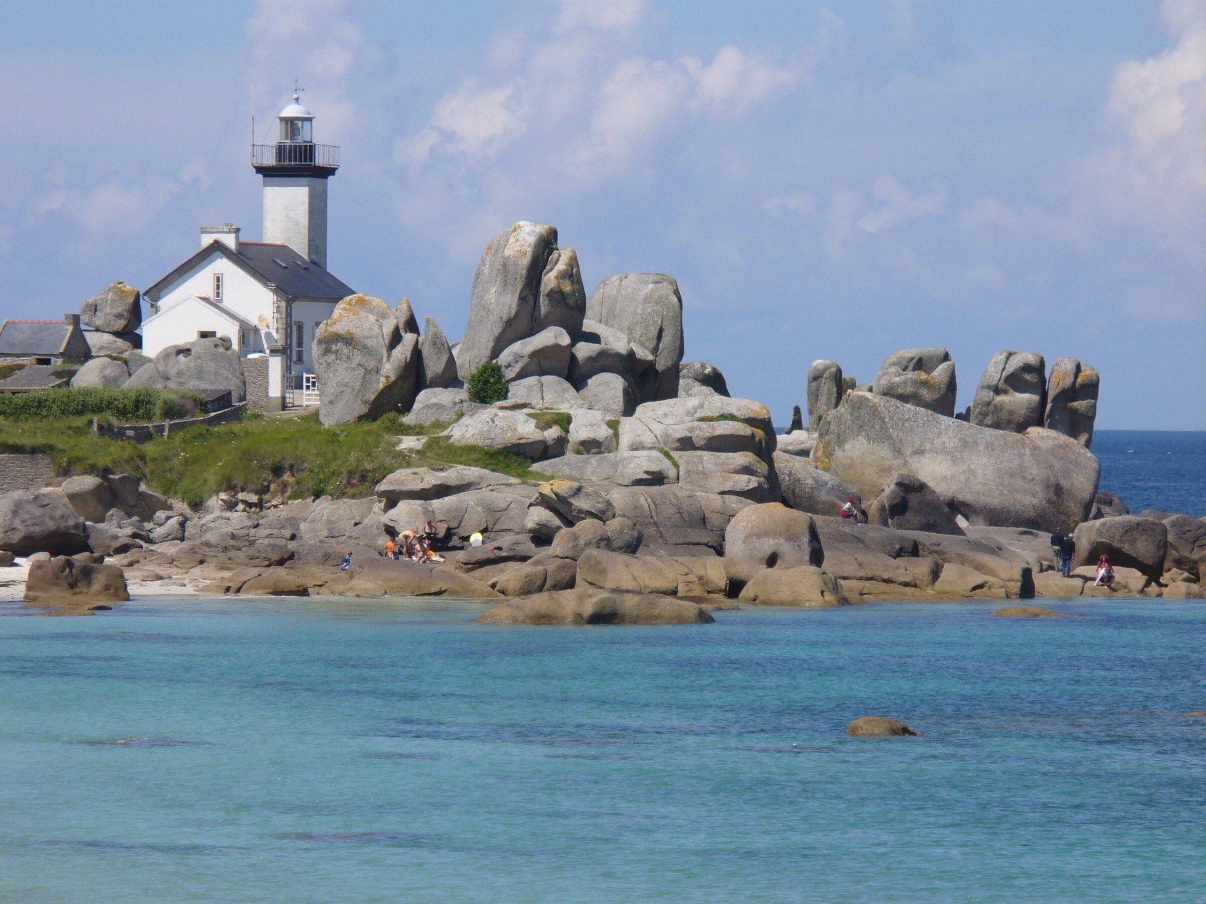 Un bâtiment situé sur la côte, doté d’un phare, entouré de gros rochers et offrant une vue sur la mer.