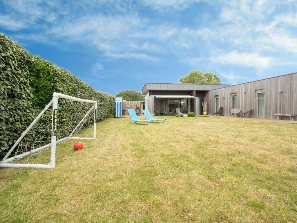 Un edificio moderno con un amplio patio cubierto de césped, un arco de fútbol y una zona de piscina.