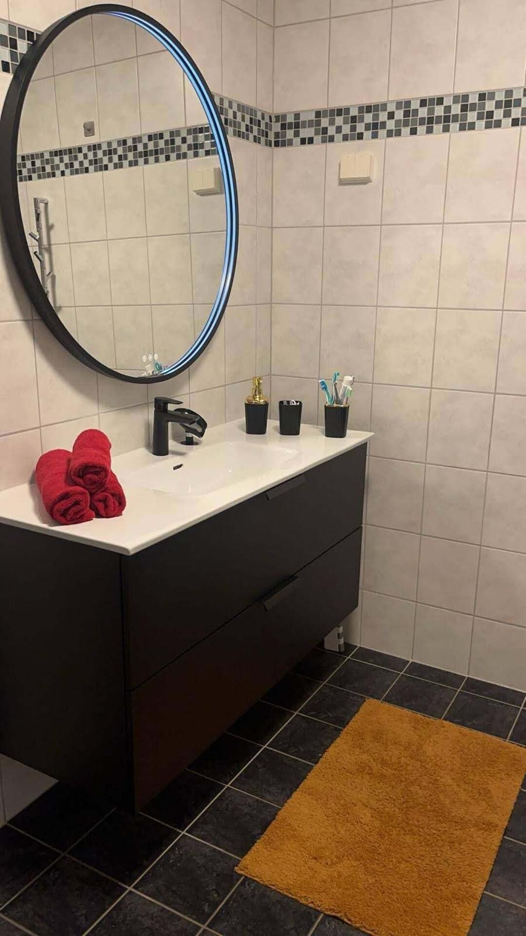 A bathroom with a white sink, black vanity, a round mirror, and a brown rug.