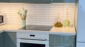 A kitchen with a microwave, stove, and cabinets. There are utensils in a container and two bottles on the counter. - Polar View Apartment (Tromsø)