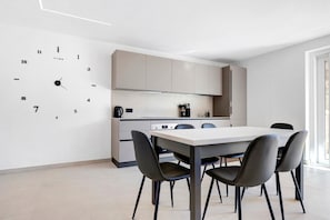 Una cucina moderna con zona pranzo, che include una sveglia a parete, pensili e un tavolo con sedie.
