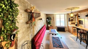 Ein rustikales Interieur mit Steinwand, Holzbalken, einer roten Bank, einem Holztisch und einer Küchenzeile mit Fenster und integrierten Geräten.