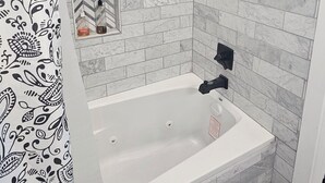 Ein Badezimmer mit einer weißen Badewanne, einer Duschbrause und einer gefliesten Wand mit Marmormuster.