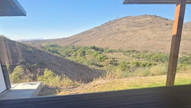 Blick aus einem Zimmer durch ein Fenster auf eine trockene, hügelige Landschaft mit spärlicher Vegetation.