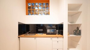 A compact kitchen with a microwave, toaster, and sink. There is a small window above the sink and a shelf with kitchen utensils.