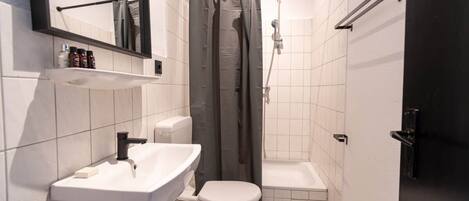 Un baño pequeño con lavamanos, inodoro y zona de ducha blancos.