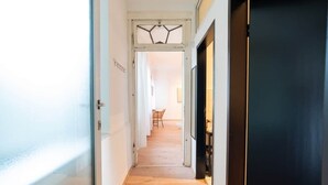 A narrow hallway with wooden flooring leading to a room with a dark door and a white ceiling.