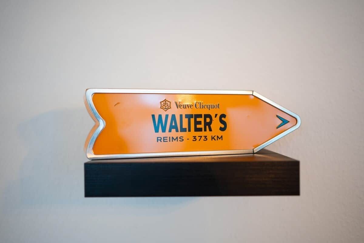 A directional sign with the text "Walter's REIMS - 373 KM" on an orange background.