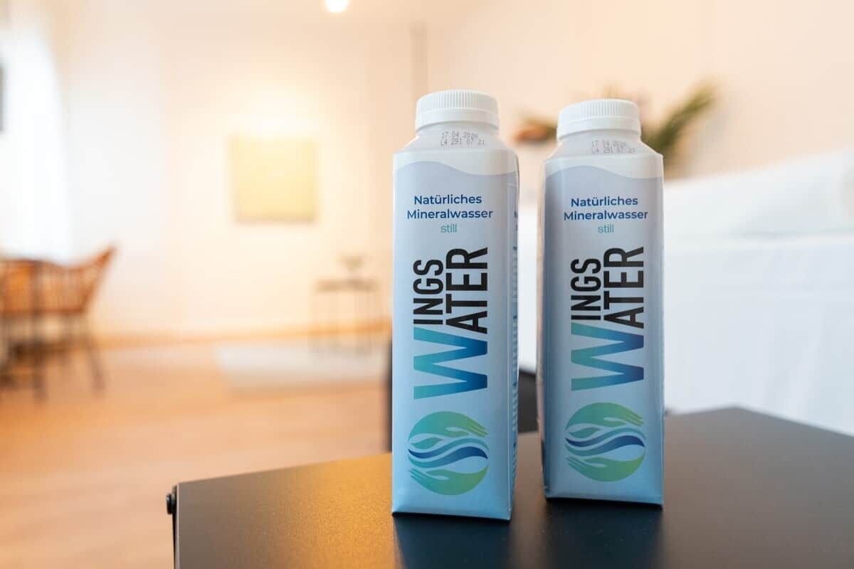Twee flessen 'WINGS WATER' mineraalwater op een tafel in een kamer met een onscherpe achtergrond.