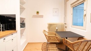 A compact kitchen with white cabinets, a black countertop, wicker chairs, and a small table.