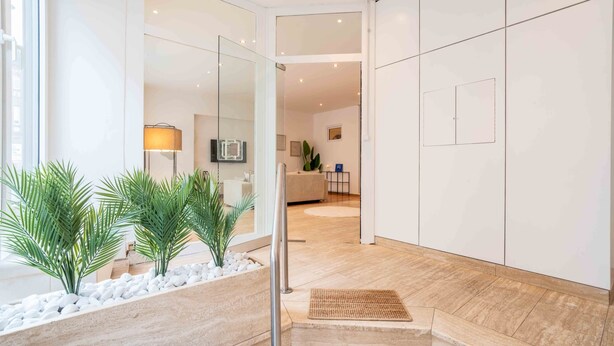 Un interior moderno con un camino de piedra que lleva a una zona de estar, un televisor de pantalla plana en la pared y un diseño minimalista con paredes blancas y suelo de madera.