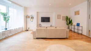 Un salón amplio con un sofá modular grande, un televisor de pantalla plana montado en la pared y una planta en maceta cerca de la ventana.