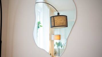 Een spiegel die een lamp en een kamer met een raam en een plantje weerspiegelt.
