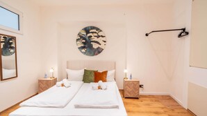Una cama doble con sábanas blancas, dos mesitas de noche con lámparas, una obra de arte en la pared y suelo de madera.