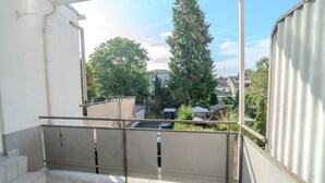 A balcony with a metal railing, a tiled floor, and a view of trees and buildings in the background. - Holiday apartment | 2 bedrooms | Sauna | Terrace (Koblenz)