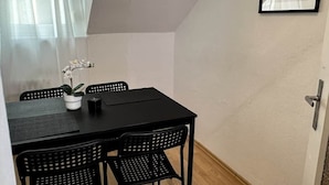 Un pequeño comedor con una mesa y sillas negras, una planta en maceta y un cuadro en la pared.