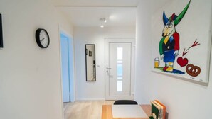 Un couloir avec une horloge, une porte, un tableau et une petite table sur laquelle sont posés des livres.