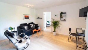Un salon moderne avec un canapé noir, un fauteuil à bascule, une petite table et une plante en pot.