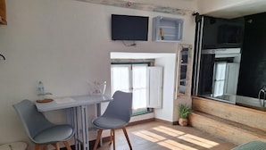 Um espaço compacto com cozinha compacta, área de refeições com duas cadeiras, uma mesa pequena e TV na parede.
