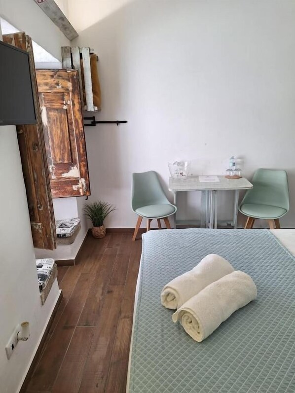Une petite pièce agréable, avec un lit, deux chaises, une table et un téléviseur fixé au mur.