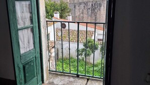Quarto com vista para uma parede de pedra antiga e um telhado de azulejos, visíveis por uma porta aberta.